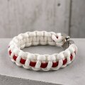 A close-up of a white and red woven paracord bracelet resting on gray stone.