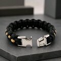 The black and gold paracord bracelet with its metal side-release buckle unlatched and resting open on a dark stone tile.