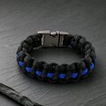 A black and blue paracord survival bracelet rests on a dark slate surface, showing the metal side-release buckle.