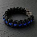 The black braided paracord bracelet with a thin blue center line lies flat on a dark stone background.
