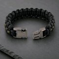 The paracord bracelet with its gunmetal buckle unclasped on a dark stone surface.