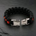 A black and orange woven paracord bracelet displayed with its silver side-release buckle unlatched on a slate backdrop.