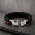 The paracord bracelet with its metal side-release buckle unlatched, resting on textured stone.