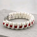 A white and red cobra-knot paracord bracelet viewed from the side on a concrete background.