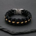 A black and gold paracord bracelet with a silver side-release buckle resting on a dark slate surface.