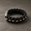 A side perspective of the black paracord bracelet featuring a thin gold center weave and a fastened silver clasp.