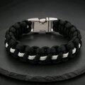 A black and white paracord bracelet with a silver side-release buckle resting on a dark slate surface, viewed from the top with the buckle centered at the back.