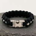 The paracord bracelet shown flat with its polished silver metal buckle fastened in the foreground on a slate surface.