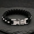 The paracord bracelet displayed with its silver metal buckle unlatched on a dark textured slate background.