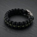 The black paracord bracelet angled on the slate surface, showing the interwoven olive green center stripe.