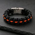 A black and orange paracord bracelet with a silver side-release buckle resting on dark slate.