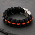 Angle view of the black and orange woven paracord bracelet featuring a metal buckle on slate.
