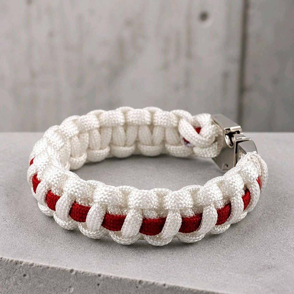 A close-up of a white and red woven paracord bracelet resting on gray stone.