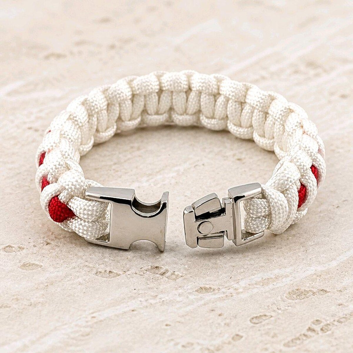 A white and red paracord bracelet with its silver metal buckle unlatched on a light stone surface.