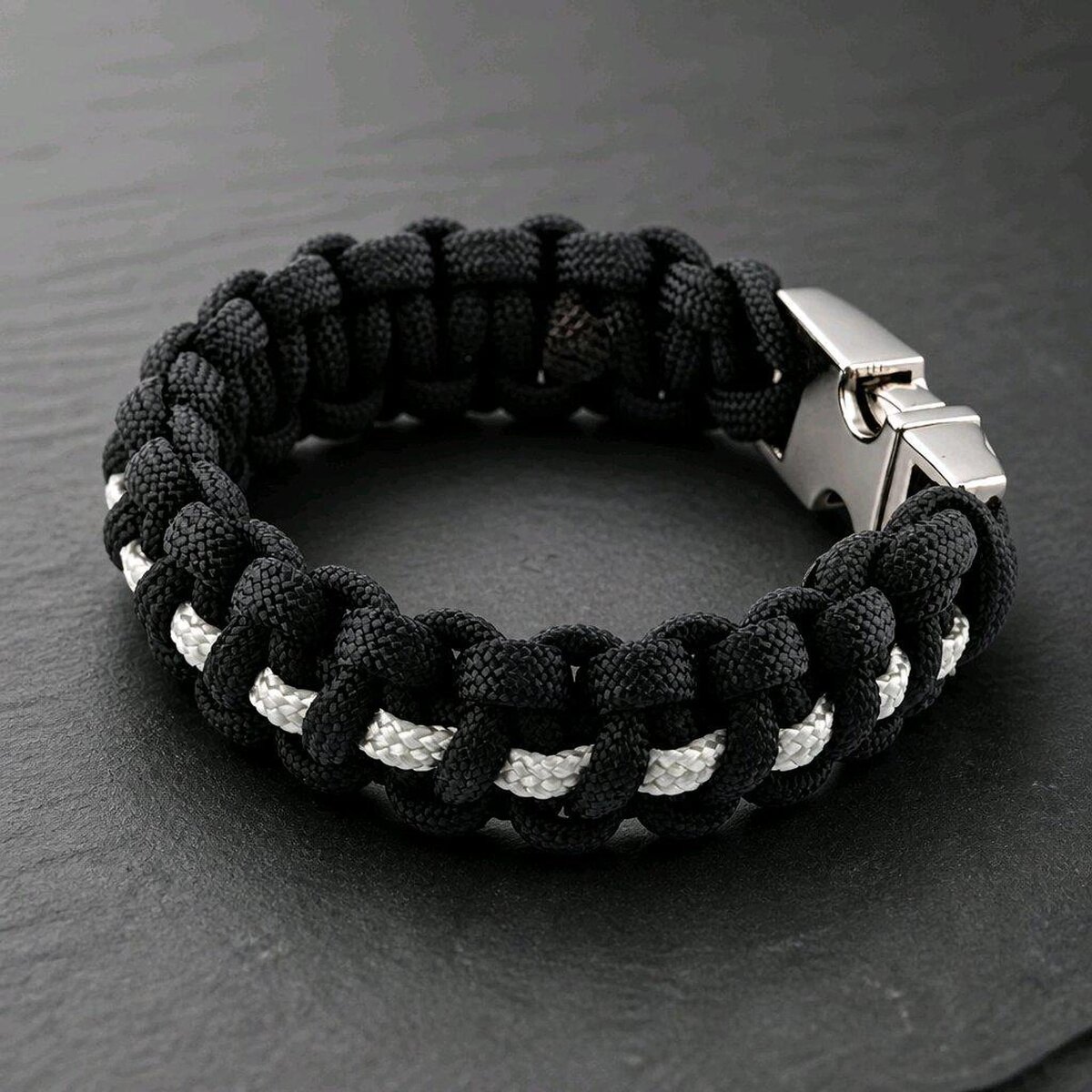 A close-up view of the black and white braided paracord bracelet on a dark slate background, angled to show the texture of the weave.