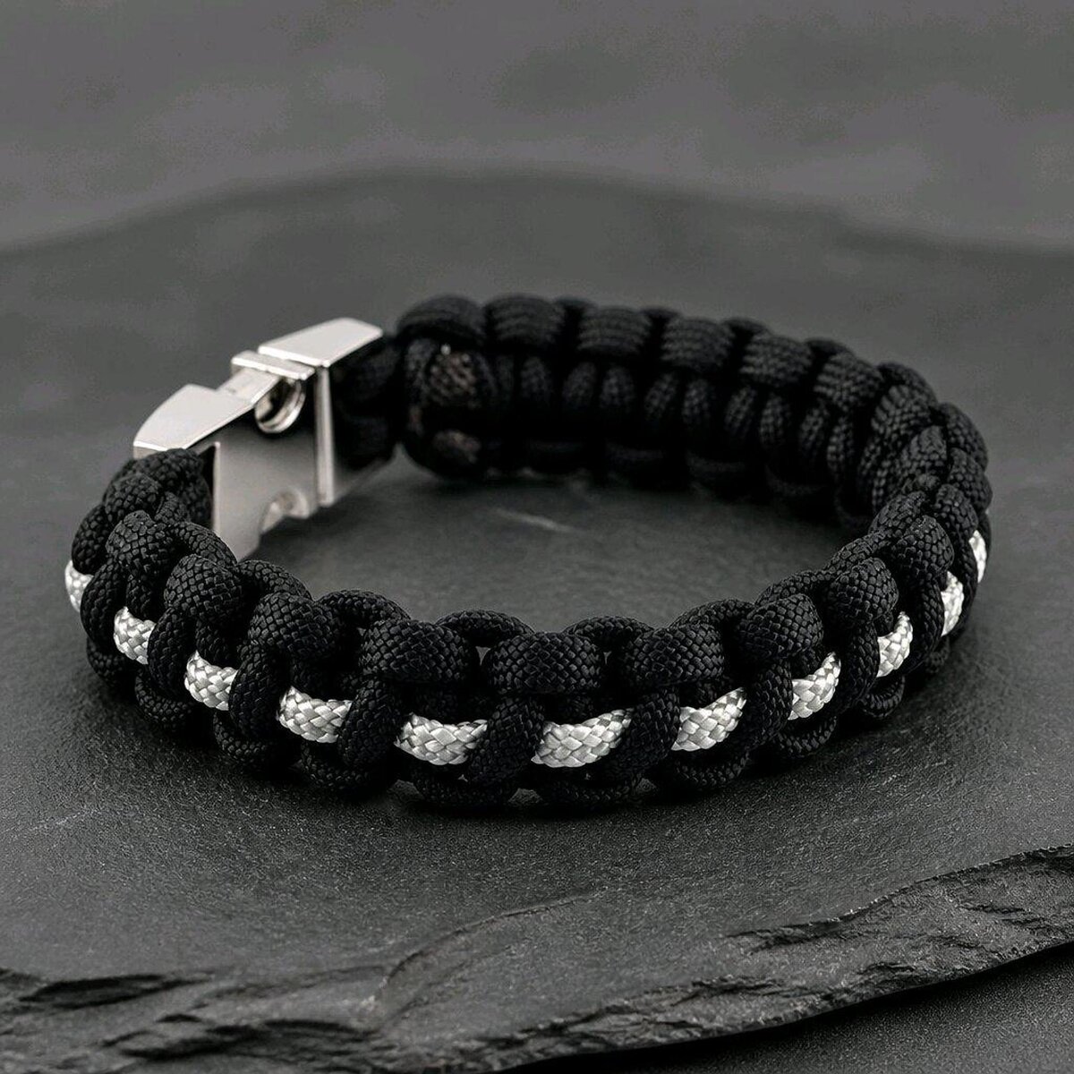 An angled view of the black and white paracord bracelet on a slate surface, focusing on the side opposite the buckle.