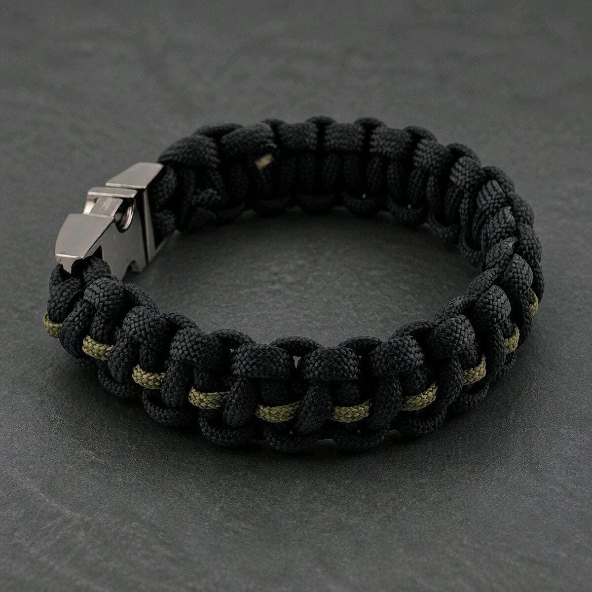 A close-up view of the paracord bracelet laid out flat on a dark textured background.