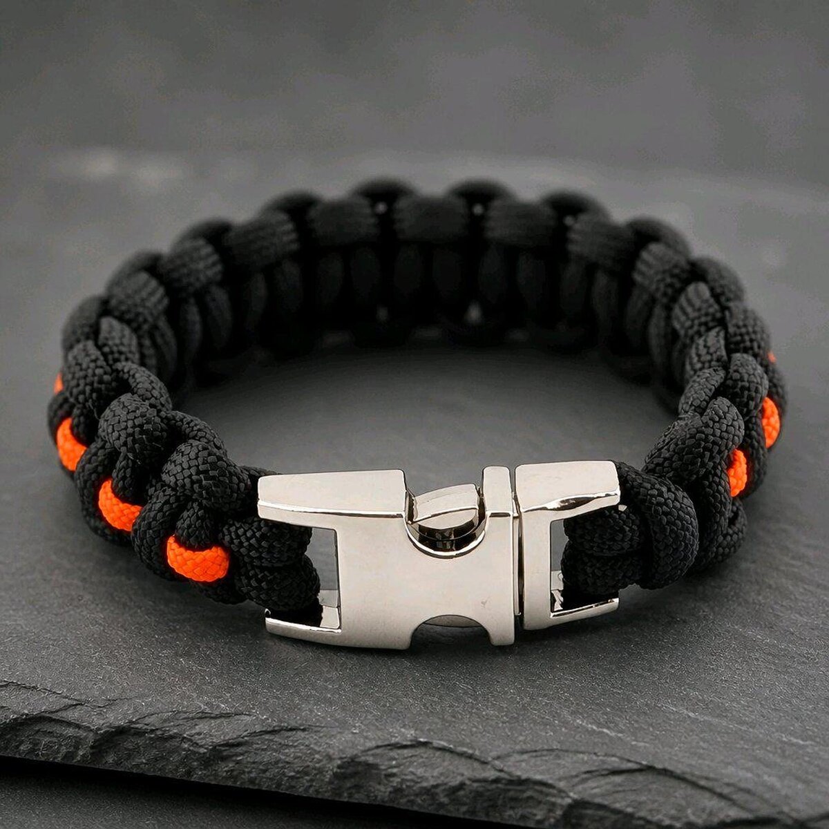 Close-up of the polished silver side-release buckle fastened on the black and orange survival bracelet.