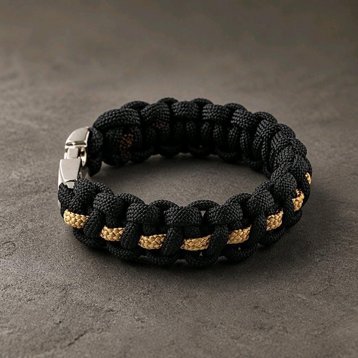 A side perspective of the black paracord bracelet featuring a thin gold center weave and a fastened silver clasp.