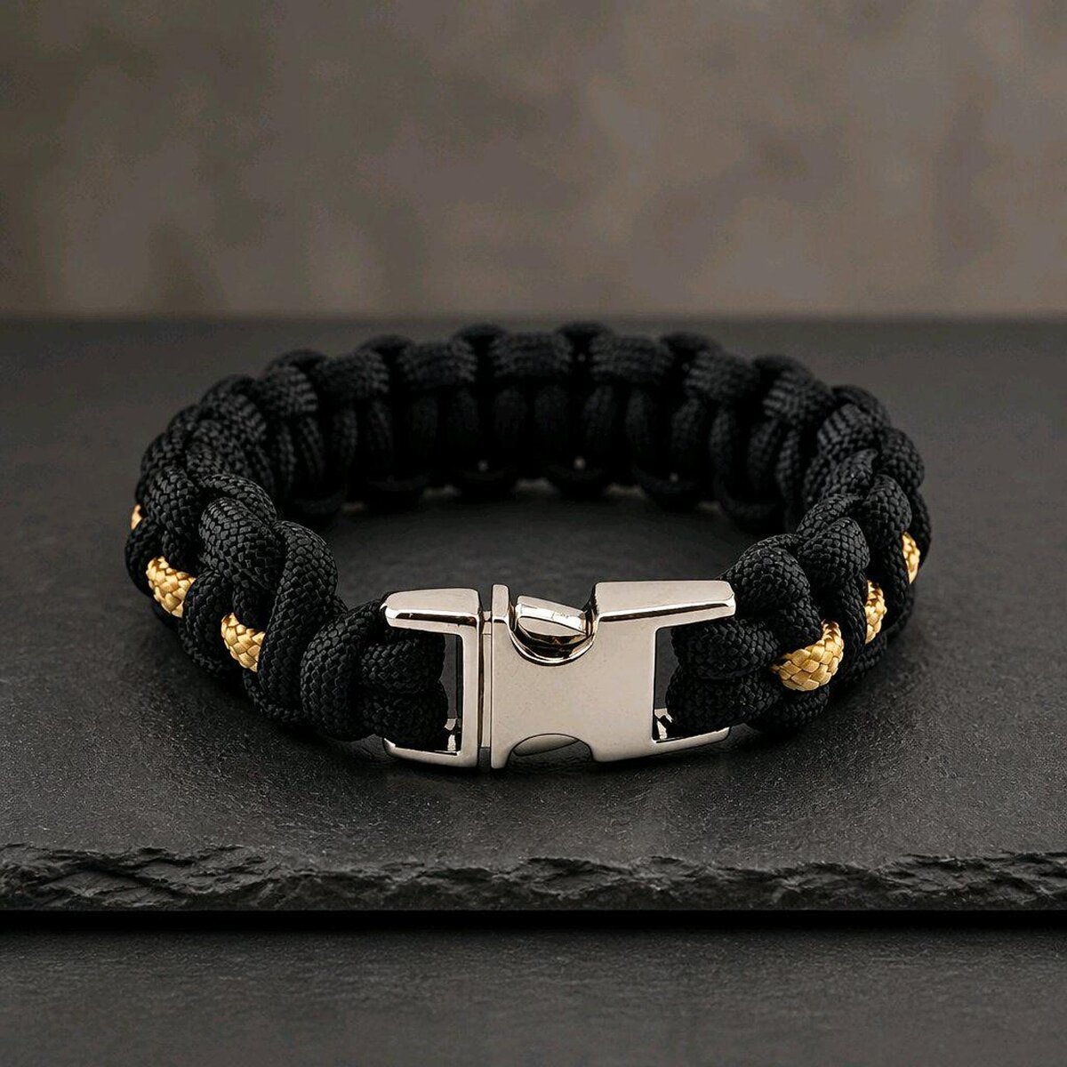 A close-up shot of the black paracord bracelet featuring a thin gold stripe down the middle and a locked silver buckle.