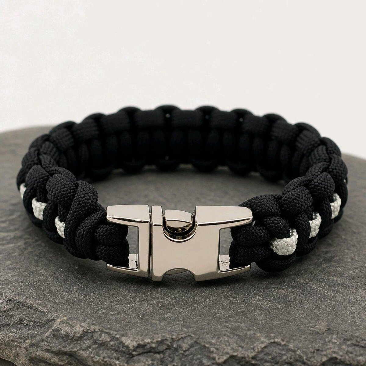 The paracord bracelet shown flat with its polished silver metal buckle fastened in the foreground on a slate surface.