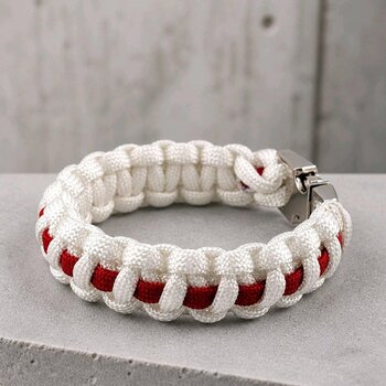 A close-up of a white and red woven paracord bracelet resting on gray stone.