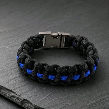 A black and blue paracord survival bracelet rests on a dark slate surface, showing the metal side-release buckle.