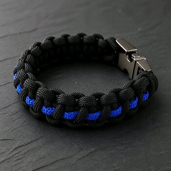 The black braided paracord bracelet with a thin blue center line lies flat on a dark stone background.