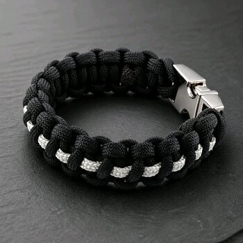 A close-up view of the black and white braided paracord bracelet on a dark slate background, angled to show the texture of the weave.