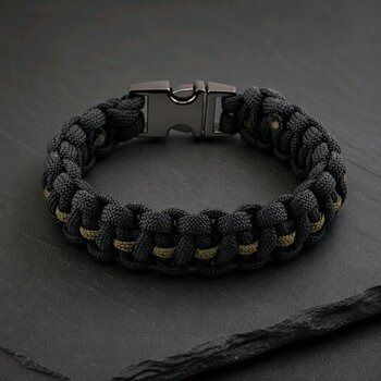 A black and olive green braided paracord bracelet with a gunmetal buckle resting on a dark slate surface.