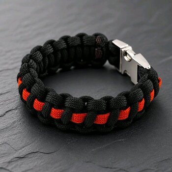 A braided black and orange paracord bracelet featuring a metal buckle, presented on a dark slate surface.