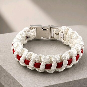 A braided white and red paracord bracelet with a silver metal buckle, resting on a textured gray surface.