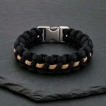 A black and gold paracord bracelet with a silver side-release buckle resting on a dark slate surface.