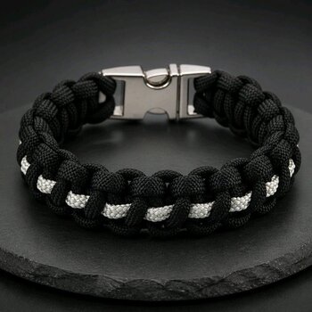 A black and white paracord bracelet with a silver side-release buckle resting on a dark slate surface, viewed from the top with the buckle centered at the back.