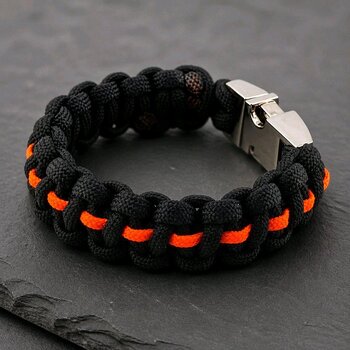 Angle view of the black and orange woven paracord bracelet featuring a metal buckle on slate.